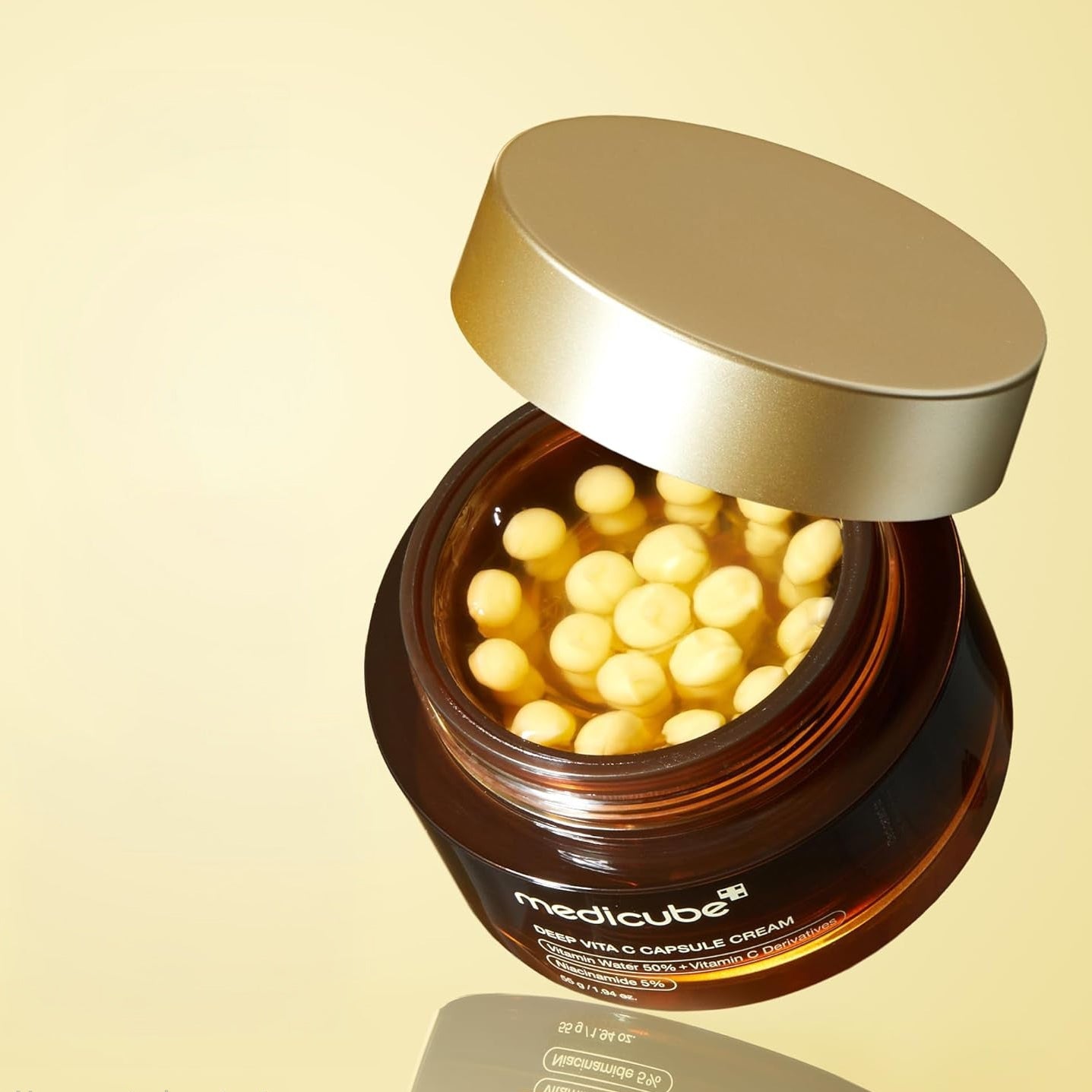Jar of medicube Deep Vita C Capsule Cream with gold cap on beige background