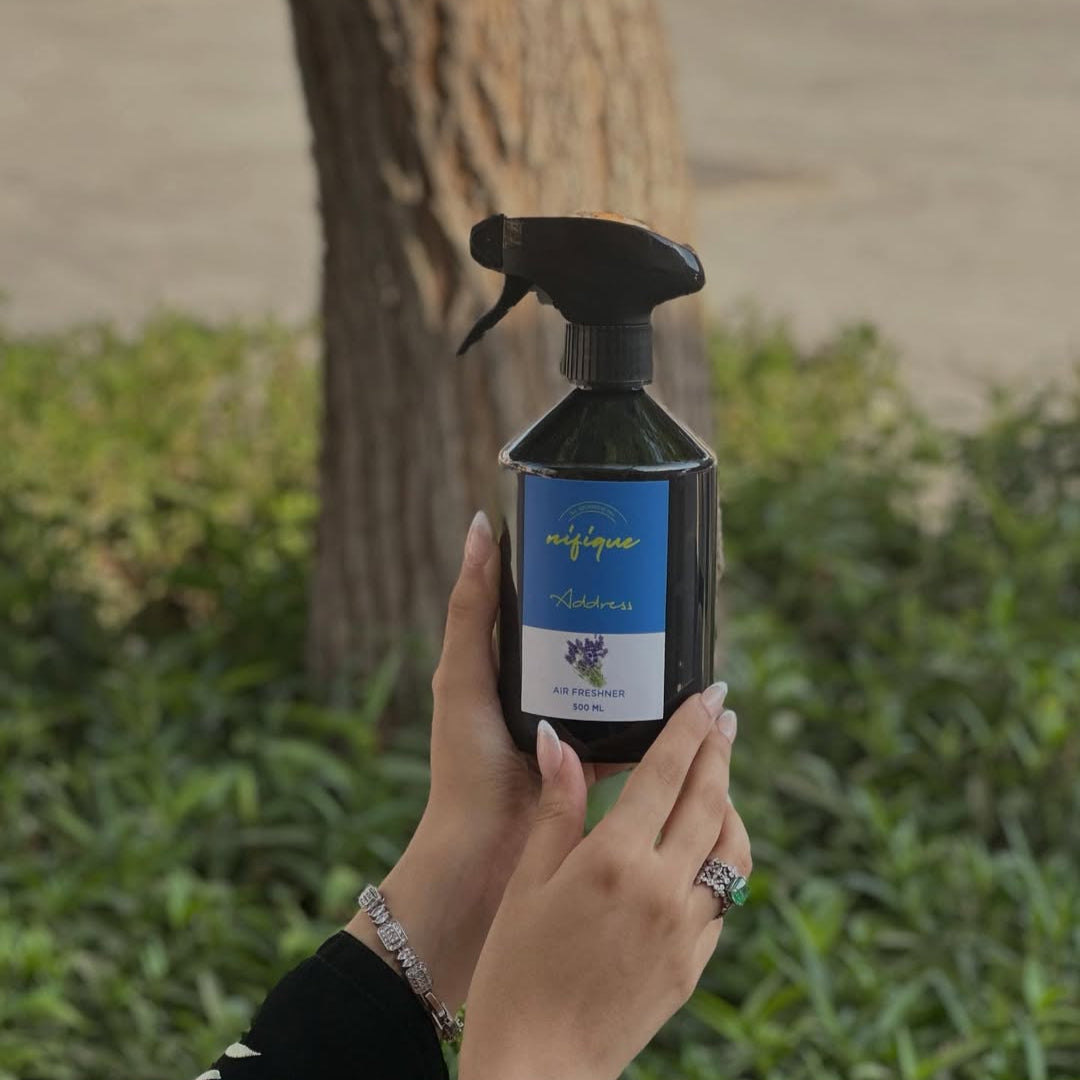 Person holding a black spray bottle with a blue label outdoors